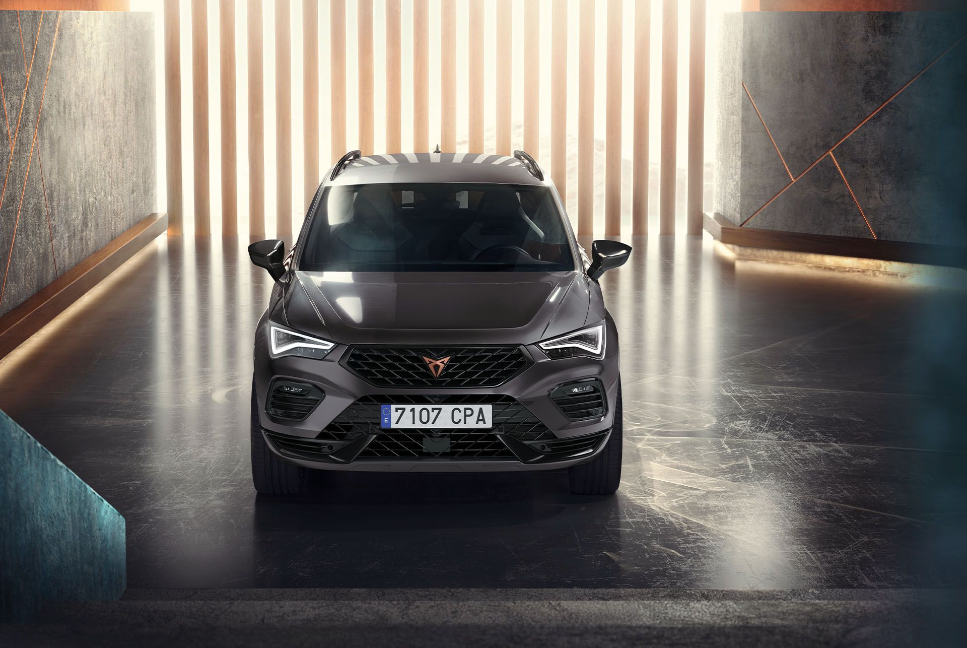 Eine Frontansicht des Cupra Ateca, eines grauen SUV, in einer modernen, beleuchteten Umgebung. Das Bild hebt den markanten Kühlergrill, die LED-Scheinwerfer und das schlanke Design des Fahrzeugs hervor. 