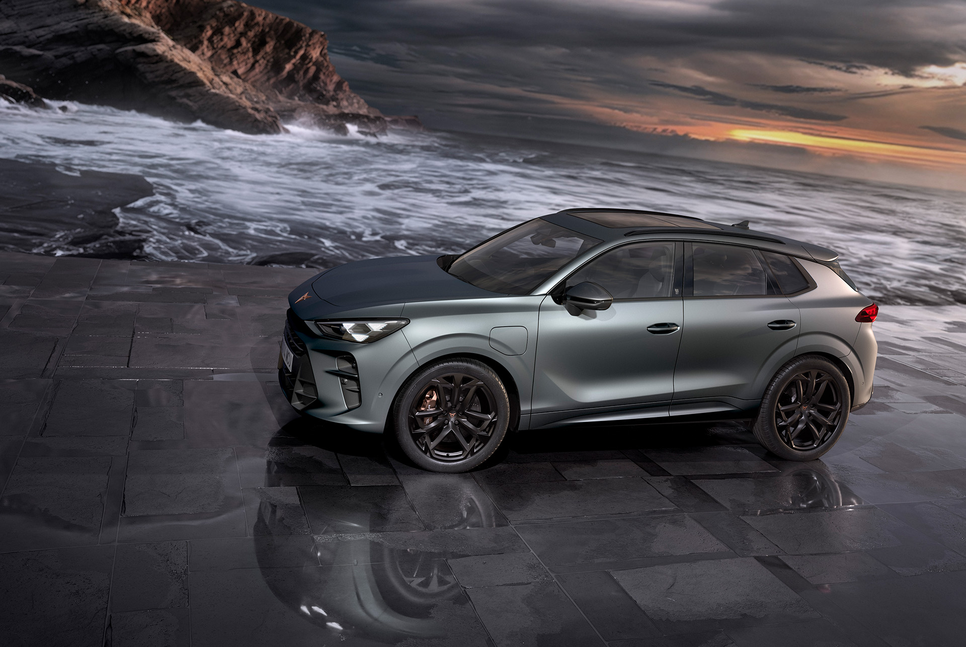 Vista laterale del SUV e-HYBRID CUPRA Terramar, nuovo modello 2024, con cerchi in lega leggera da 20” America’s Cup e freni Akebono, Enceladus Grey opaco, su terreno bagnato al mare al tramonto. 